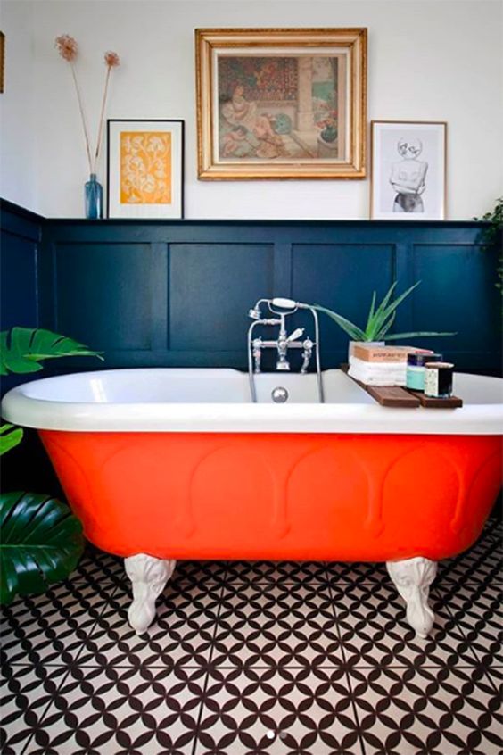 a moody bathroom with black paneling, a contrasting tile floor, an orange bathtub, potted plants and some art and books
