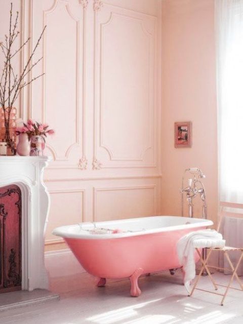 a lovely girlish bathroom with blush paneled walls, a vintage fireplace, a pink clawfoot bathtub, a shabby chic chair and some blooms