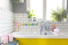 28 a fun and cheerful bathroom with white subway and tan and white tiles, a yellow clawfoot bathtub, potted plants, touches of pink and bold colors