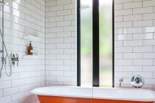 29 a laconic bathroom with a plywood ceiling, white tiles on the walls, a concrete floor, an orange clawfoot bathtub and a window with frosted glass