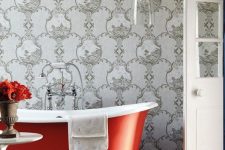 31 a refined bathroom with grey printed wallpaper, a stained floor, a red free-standing bathtub, a glass pendant lamp over the tub