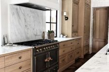 a beautiful and refined kitchen with light-stained cabinetry, a white hood and a white marble backsplash plus countertops