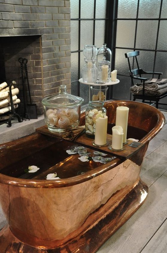 a beautiful bathroom with a non-working fireplace, elegant furniture, a copper bathtub and candles all around