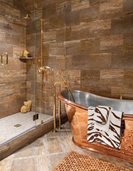 a beautiful bathroom with tan and greige tiles, a cool shower space enclosed in glass, a shiny copper bathtub with a stainless steel inner is amazing