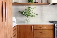 a beautiful mid-century modern kitchen with stained cabinets, a white tile backsplash and white countertops, greenery for a fresh look