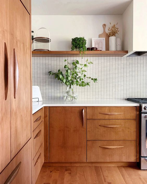 a beautiful mid century modern kitchen with stained cabinets, a white tile backsplash and white countertops, greenery for a fresh look