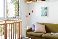 a beautiful mid-century modern nursery with open box shelves, a stained round crib, a green sofa, artworks, bright toys that double as decor