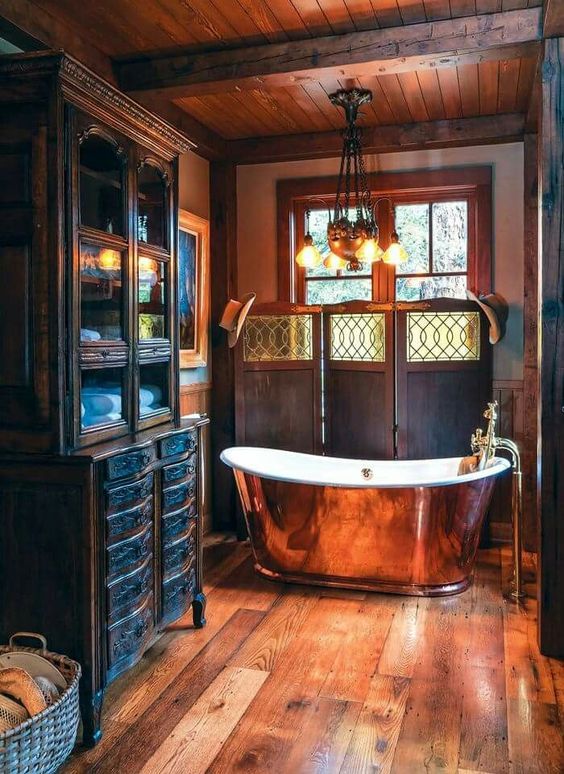 a beautiful vintage bathroom clad with stained wood, with a large vintage buffet, a copper bathtub and a window that still keeps privacy due to the screen