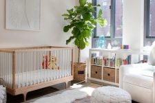 a beautifully styled nursery features a framed angel wings are piece fixed to a pale pink wall over a mid-century modern crib