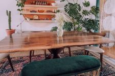 a boho mid-century modern dining room with a round orange shelving unit, a stained table, stained chairs and a green upholstered bench plus various plants