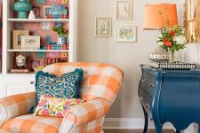 a bright living room with a bookcase with bright lining, a vintage blue credenza, a bright checked chair with a matching footrest and a mirror with a pretty frame