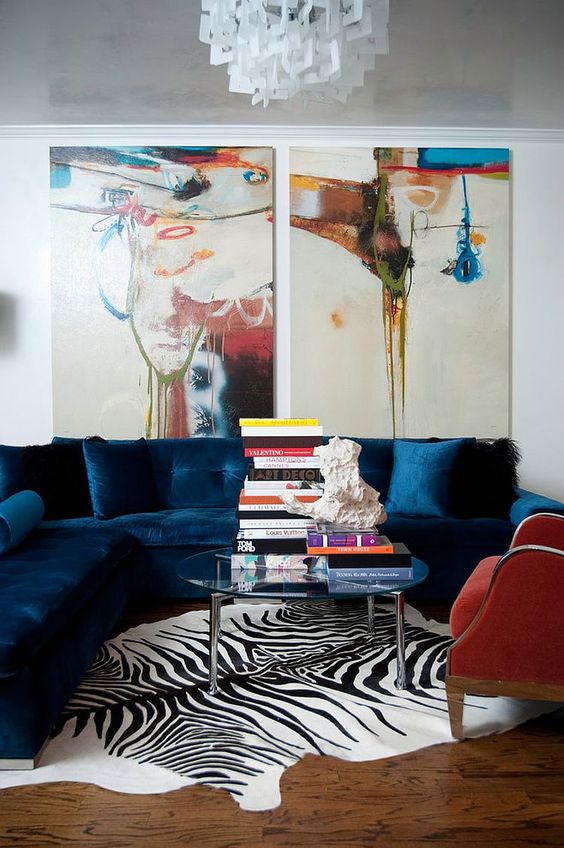 a bright living room with a navy sectional, a red chair, a clear glass coffee table, bold artwork and a zebra print rug is amazing