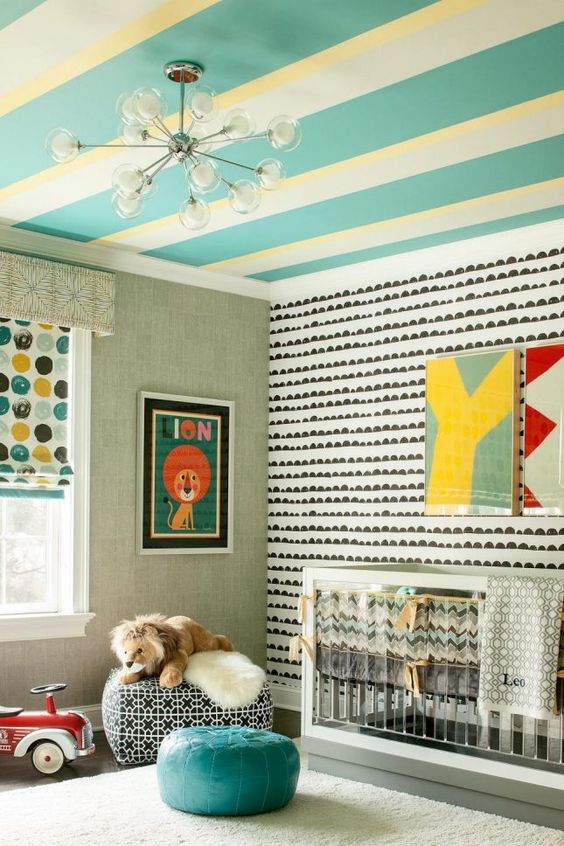 a bright mid-century modern nursery with a yellow and turquoise striped ceiling, an accent wall, an acrylic crib, poufs, bright artwork