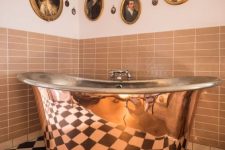 a checked black and white floor, rust tiles on the walls, a polished copper bathtub and a vintage gallery wall of oval and round artworks