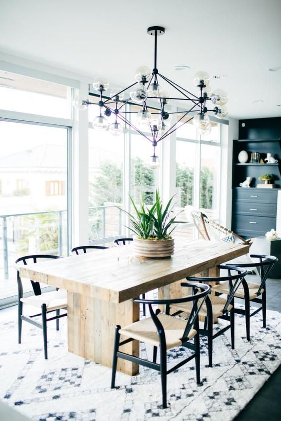 a chic mid-century modern dining space with a stained table and black and white chairs, a printed rug, a black storage unit and a large and cool chandelier