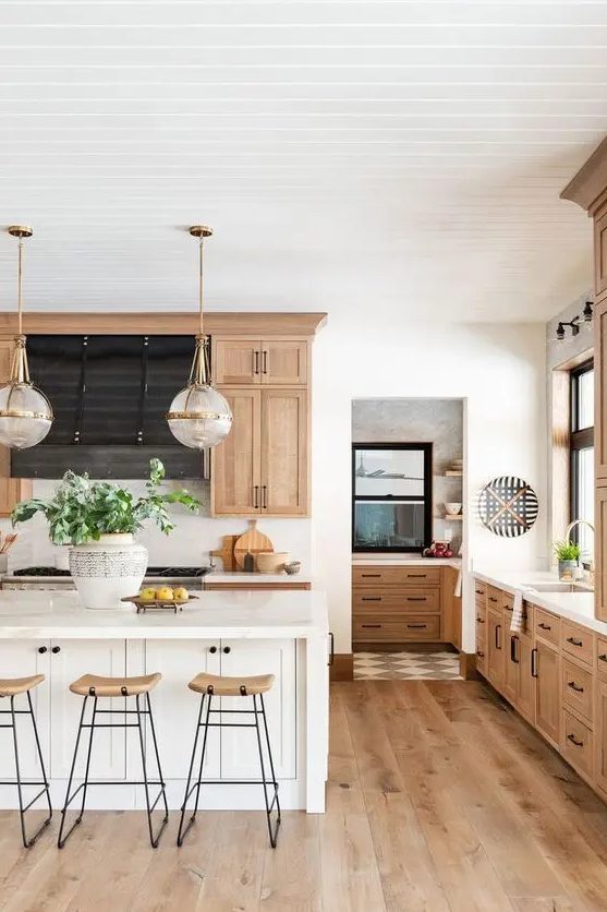 a chic modern country kitchen with light stained cabinets and hardwood floors, a white kitchen island, tall stools and pendant lamps