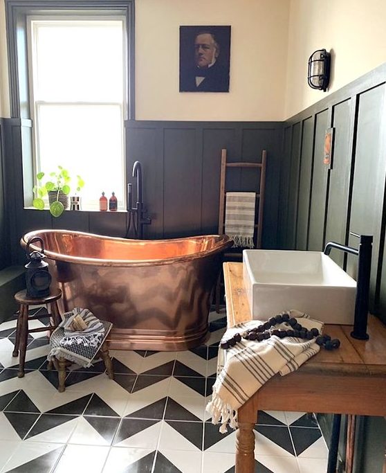 a chic vintage bathroom with black paneling, chervon tile floor, a copper bathtub that brings a touch of color here