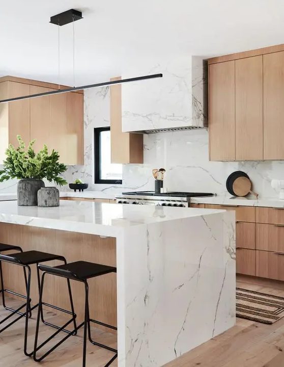 a contemporary kitchen with elegant light-stained cabinets, a white stone hood and countertops plus a bakcsplash and a matching kitchen island