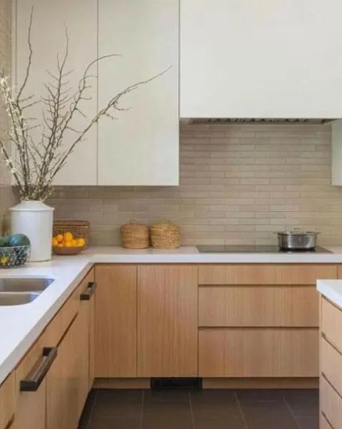 a contemporary neutral kitchen with ivory and light stained cabinets, a brick backsplash, white countertops and black handles is very chic