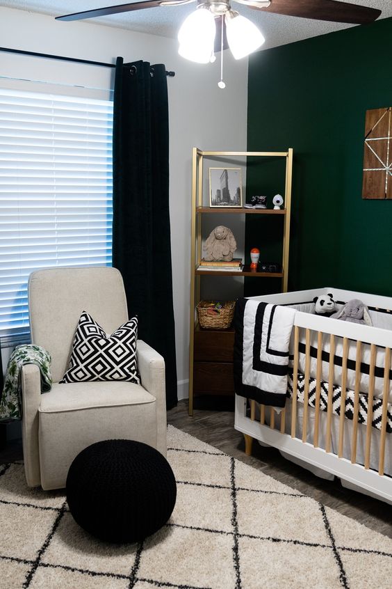 a contrasting mid-century modern nursery with a dark green accent wall, a gold shelving unit, a neutral crib, a grey chair, a black pouf and black and white textiles