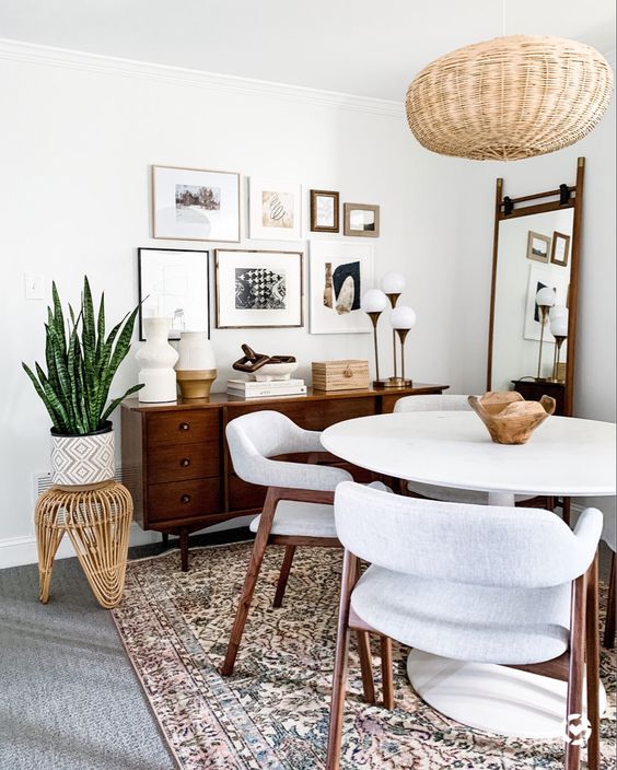 a cozy mid-century modern dining nook with a stained credenza, a white round table and chairs, a woven pendant lamp and a gallery wall