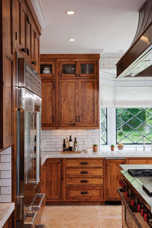 a cozy rustic kitchen with rich-stained cabinets, white subway tiles, white stone countertops and black handles is a welcoming space