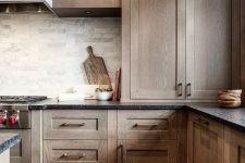 a dark-stained kitchen with shaker style cabinets, black stone countertops, a grey marble tile backsplash and open shelves