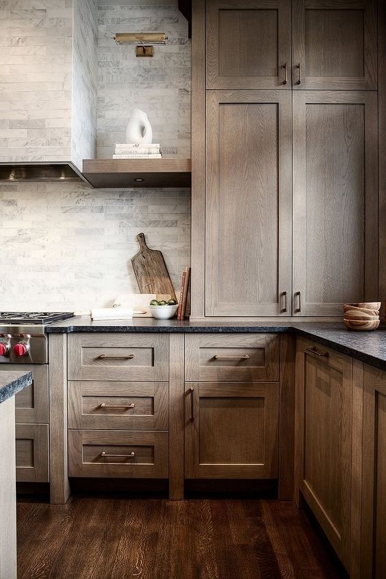 a dark-stained kitchen with shaker style cabinets, black stone countertops, a grey marble tile backsplash and open shelves