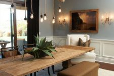 a dining space with paneling, with a large vintage rustic dining table, stylish taupe benches and mid-century modern chairs plus an industrial meets rustic chandelier