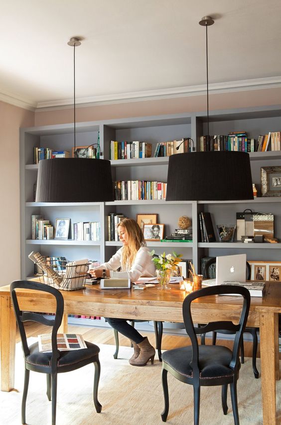 a home office with a grey storage unit, a large rustic table and vintage black chairs and black pendant lamps is amazing