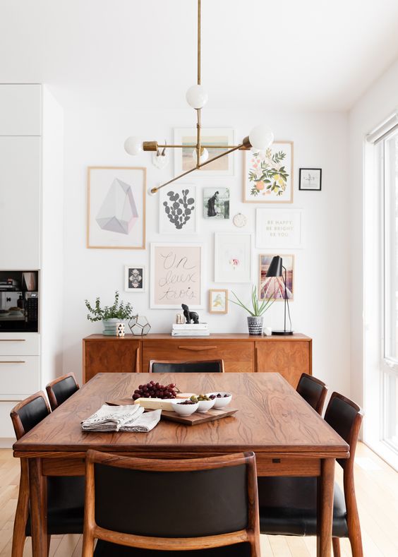 a light-filled mid-century modern dining nook with a stained credenza and table, black chairs, a classic chandelier and a gallery wall