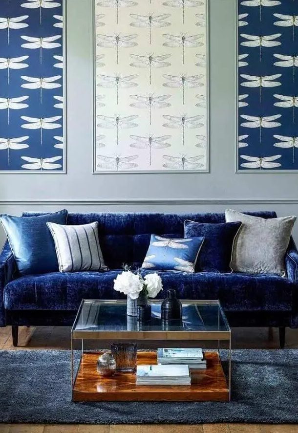 a living room with an electric blue sofa, printed pillows, a gallery wall of wallpaper, a tiered coffee table and a midnight blue rug
