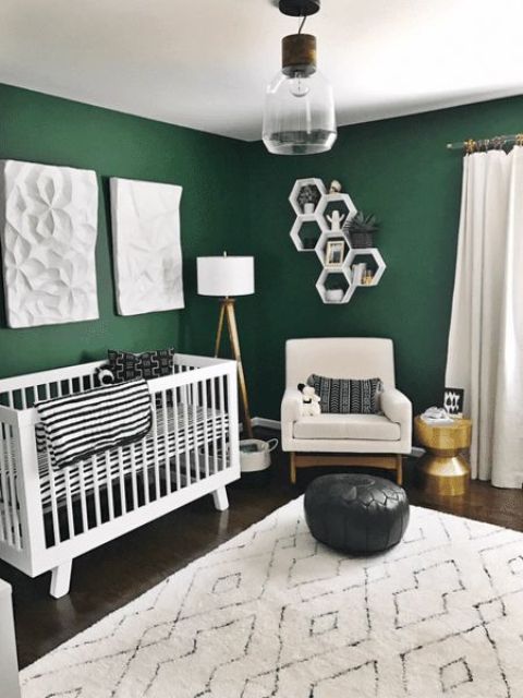 a lovely mid-century modern nursery with green walls, a white crib, a creamy chair, a black pouf, black and white textiles, hexagon shelves and a pendant lamp