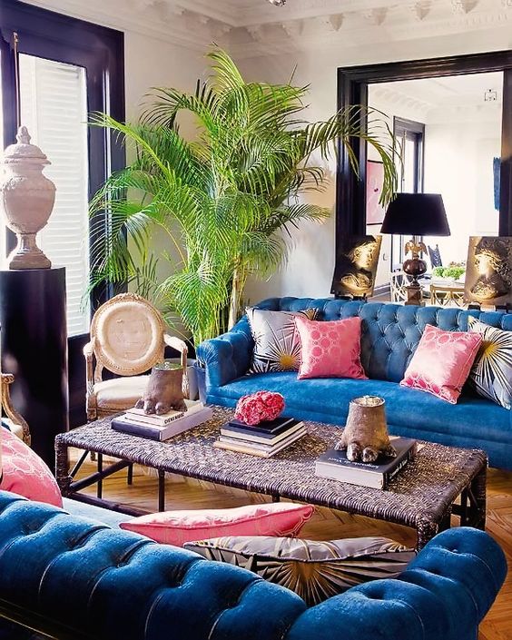 a maximalist living room with black window and door frames, blue sofas, a chic woven coffee table and a potted tree is wow