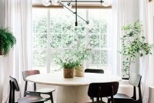 a mid-century modern dining spot with a white round table, black chairs, potted plants and a black chandelier is cool