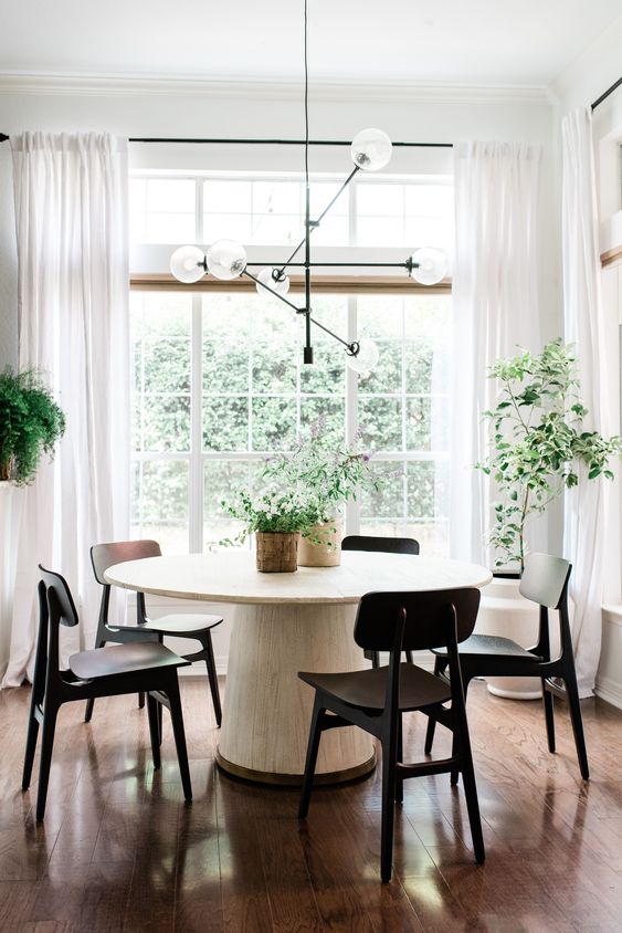 a mid century modern dining spot with a white round table, black chairs, potted plants and a black chandelier is cool