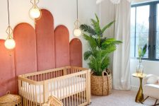 a mid-century modern nursery with coral upholstery on the wall, a stained crib, baskets, a pink ceiling, layered rugs and greenery
