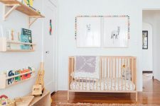 a mid-century modern nursery with stained open shelves, a wooden crib, a bright printed rug, printed bedding, artwork and bright decor and toys