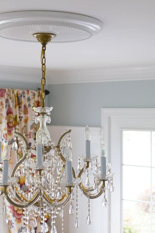 a modern sleek ceiling medallion complemented with a super chic vintage chandelier with crystals hanging down and faux candles
