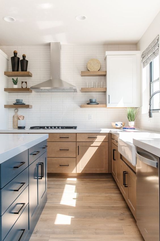 a modern farmhouse kitchen with light stained cabinets, a navy kitchen island, white stone countertops and a skinny tile backsplash, black handles