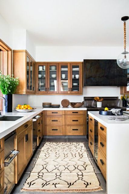 a modern farmhouse kitchen with stained cabinets, a black hood and black appliances, white stone countertops and a white backsplash