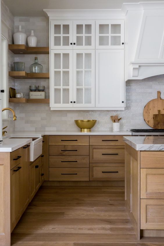 a modern farmhouse kitchen with upper white cabinets and lower stained ones, neutral tiles and corner shelves plus brass for a chic touch