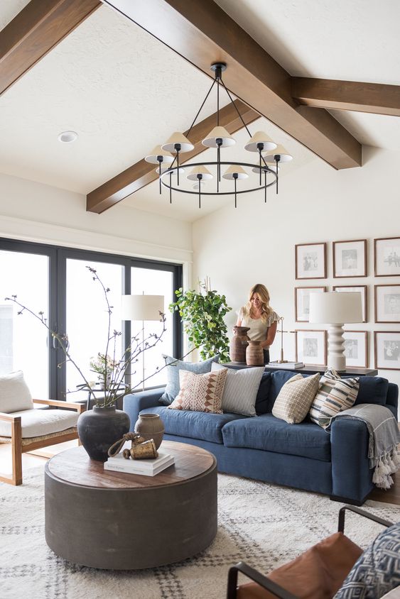 a modern farmhouse neutral living room with a blue sofa, a gallery wall, a round coffee table and mismatching chairs, a stylish chandelier