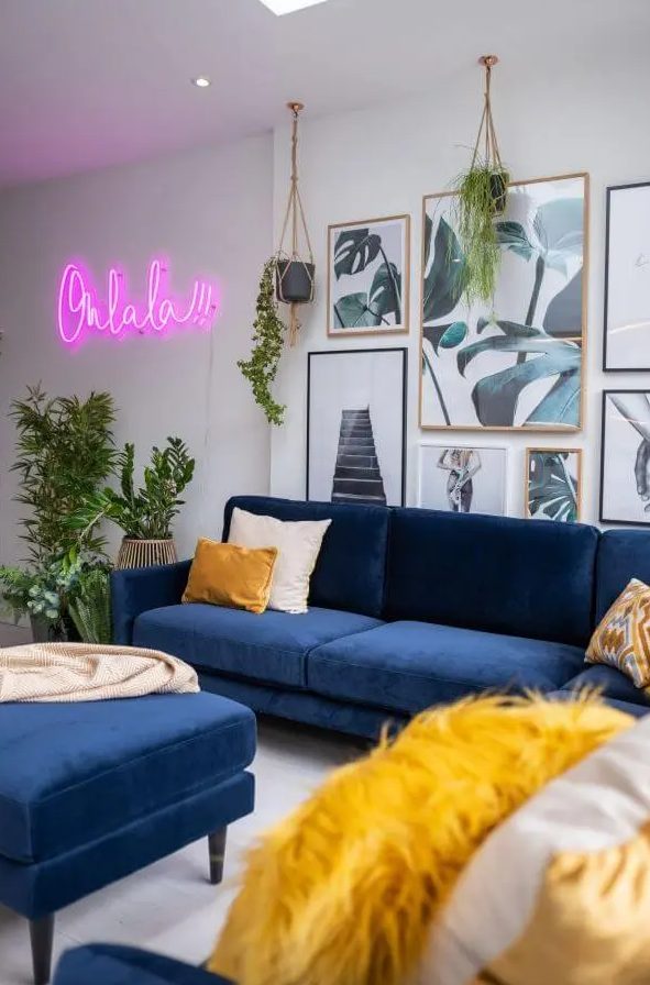 a modern living room with navy sofas, an ottoman, a botanical gallery wall, potted greenery and a pink neon sign on the wall