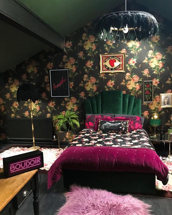 a moody attic bedroom with dark floral wallpaper, a chic mid-century modern to art deco upholstered bed with bright bedding, a vintage console table