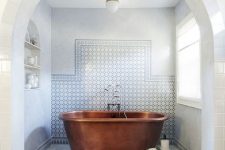 a neutral Moroccan bathroom with marble tiles, a round stool, a niche with shelves, a round lamp with much natural light