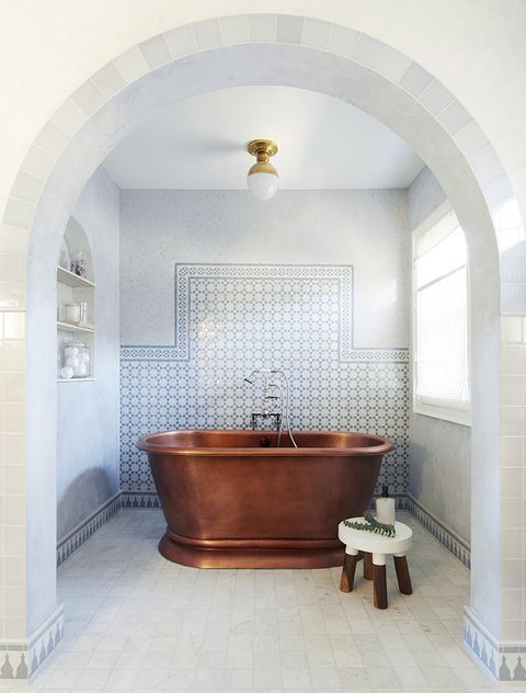 a neutral Moroccan bathroom with marble tiles, a round stool, a niche with shelves, a round lamp with much natural light