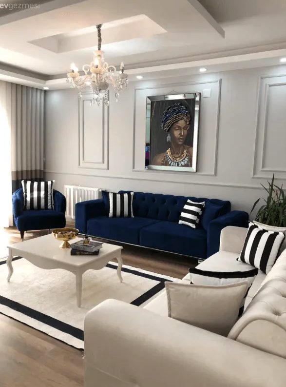 a neutral living room with a navy sofa and chair, a creamy sofa, a vintage coffee table and striped pillows and a rug plus a chic crystal chandelier