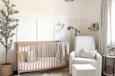 a neutral mid-century modern nursery with a stained crib, a white chair and a pouf, paneled walls, neutral textiles, a potted tree