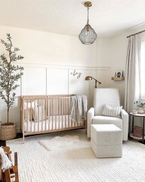 a neutral mid century modern nursery with a stained crib, a white chair and a pouf, paneled walls, neutral textiles, a potted tree